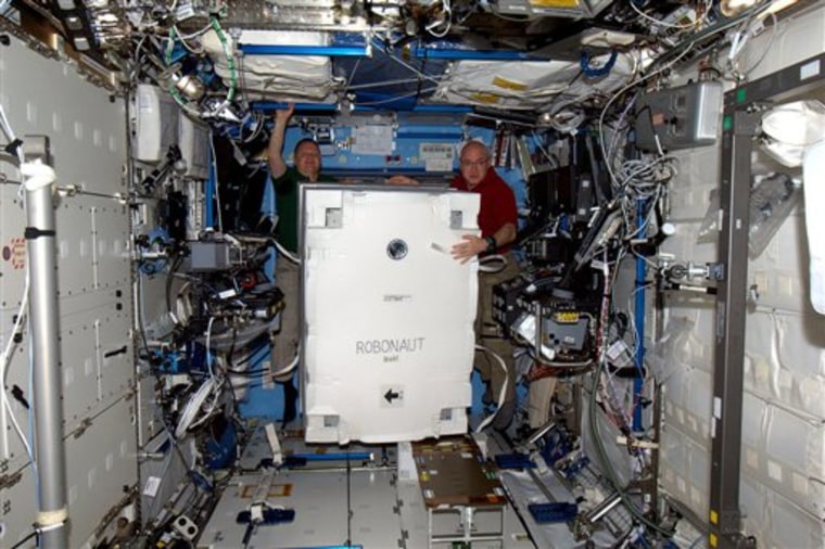 In this March 3, 2011 photo provided by NASA, astronauts Eric Boe, left, and Scott Kelly move the crate containing Robonaut 2, better known as R2, the first humanoid robot in space, at the International Space Station. The 220-mile-high (354-kilometer-high) unveiling of R2, the first humanoid robot in space, is being moved up at the urging of the president of the United States. Astronaut Catherine Coleman said Friday, March 4, 2011 that she and the 11 other humans aboard the shuttle-station complex want to get R2 out of its packing material as soon as possible. R2, flew to the International Space Station aboard Discovery and will stay behind when the shuttle leaves Monday. (AP Photo/ESA/NASA)